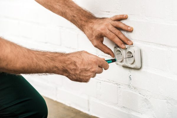 cropped image of electrician repairing power socket with screwdriver at home
